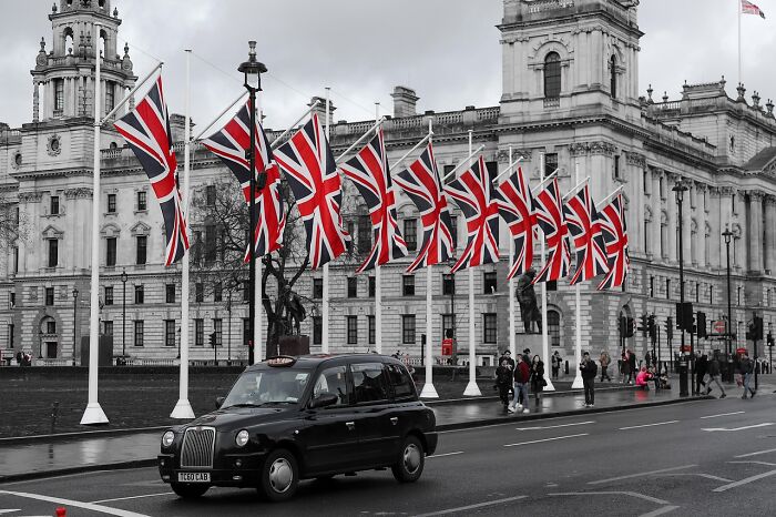 Black London taxi driving past UK flags on poles in front of historic government building for cognitive ability test concept.