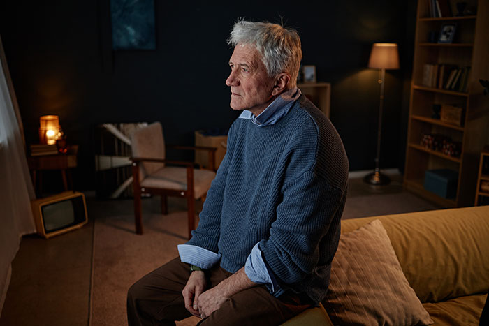 Elderly man in a blue sweater sitting thoughtfully in a dimly lit room after seeing something unexplainable.