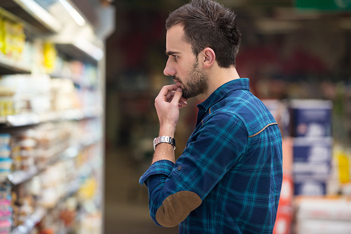 Man in a blue plaid shirt thoughtfully examining products on a store shelf, experiencing something unexplainable.