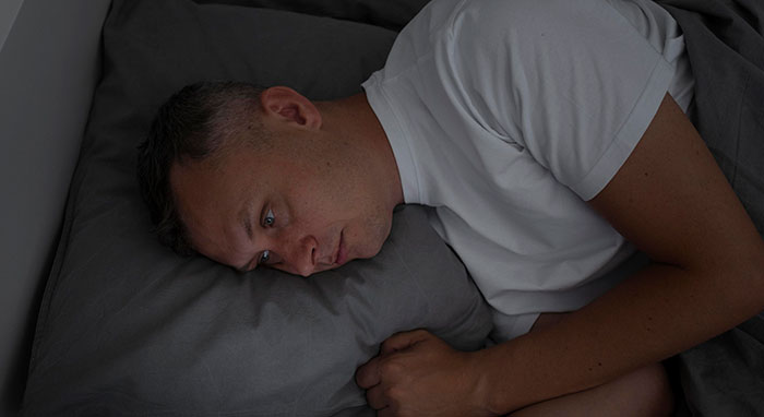 Man lying awake in bed, wide-eyed and unsettled, experiencing an unexplainable moment that feels like reality.