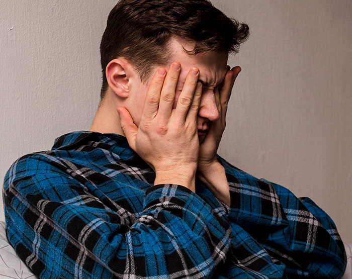 Young man in a blue plaid shirt covering his face, appearing shocked after seeing something unexplainable.