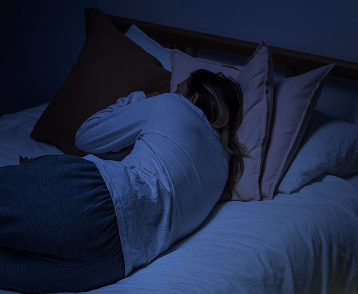 Person lying asleep in bed at night, evoking a scene related to seeing something unexplainable.