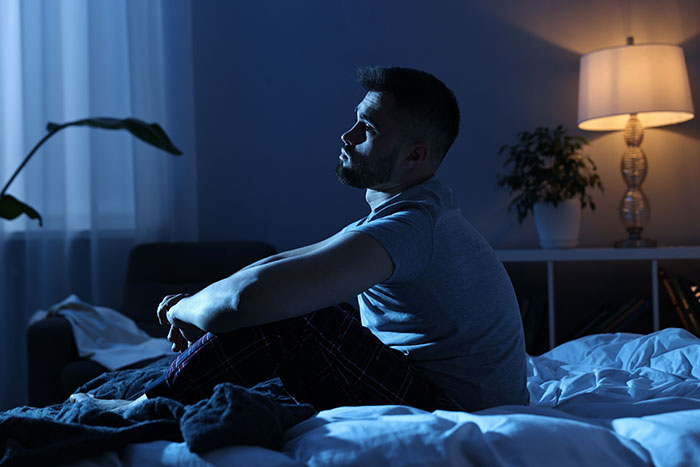 Man sitting on bed at night, looking thoughtful and unsettled after seeing something unexplainable and vivid.