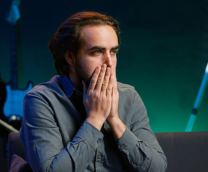 Man with hands covering mouth, looking shocked and confused after witnessing something unexplainable in a dimly lit room.