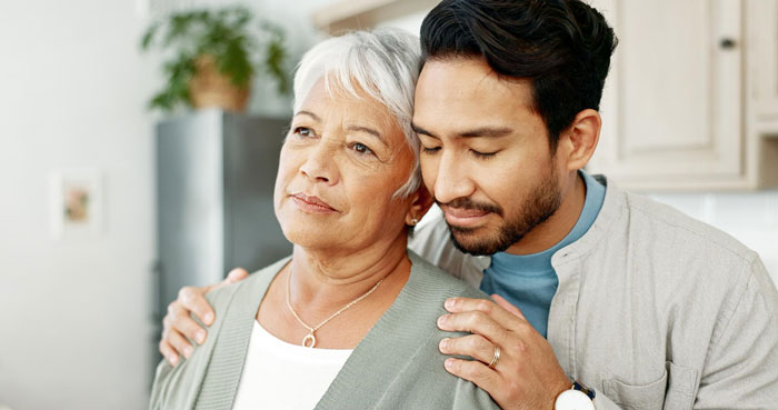 Young man gently comforting overbearing mother-in-law as daughter-in-law puts her foot down on plans made without her.