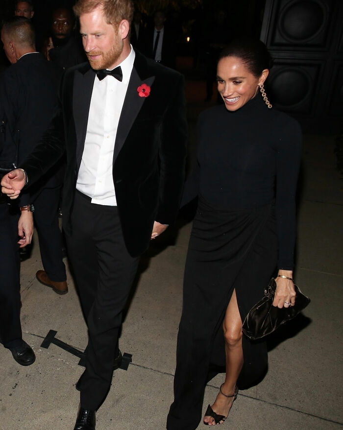 Prince Harry and Meghan Markle walking together at a nighttime event, dressed in formal black attire.