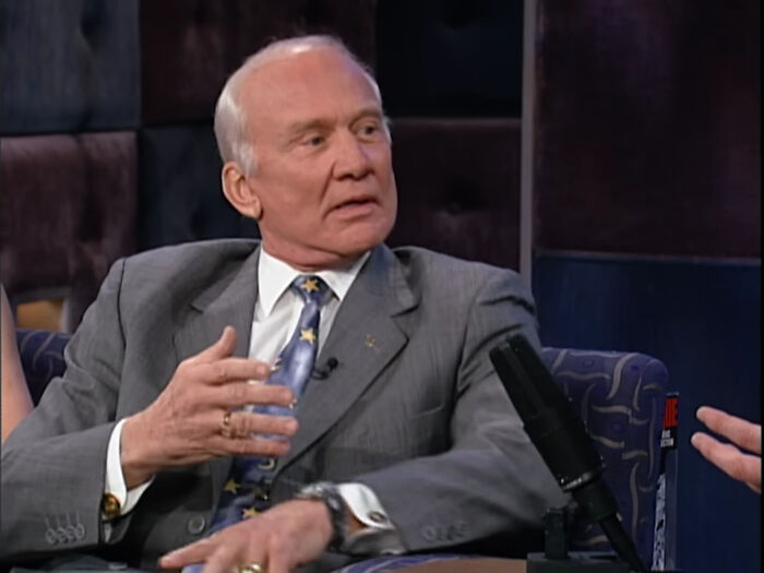 Elderly man in a suit discussing moments people met their idols and experienced regret during a talk show interview.