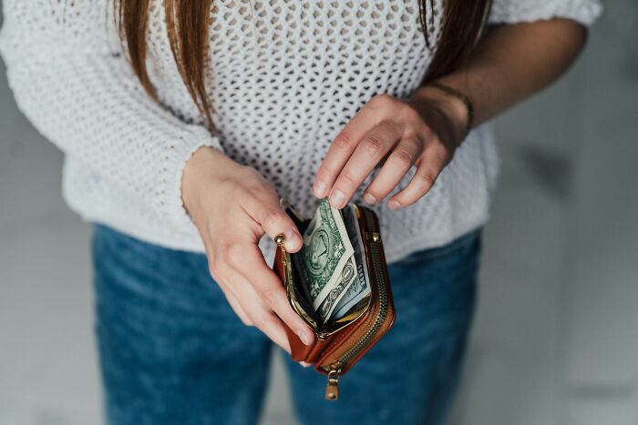Person holding a brown wallet with folded US dollar bills, illustrating economic issues affecting America at the moment.