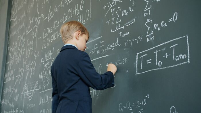 Young boy solving complex math problems on a chalkboard showing surprising intelligence and advanced knowledge.