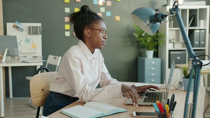Young woman working on a laptop in a home office, focusing on adult goals and planning tasks at her desk.