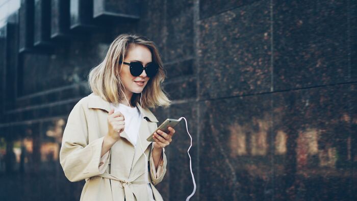 Woman in sunglasses using phone outdoors, demonstrating common things women do to feel safer while living alone.