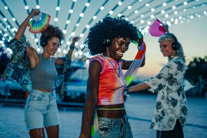 Three women dancing outdoors at night wearing headphones, enjoying music while practicing safety tips for living alone.