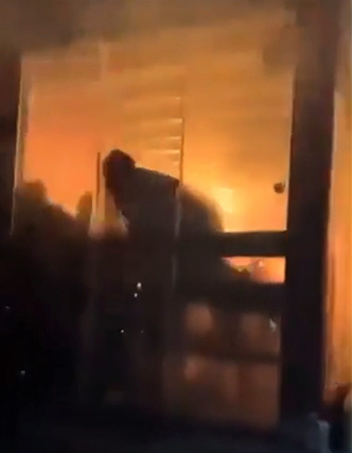 Silhouette of a person escaping through a window amidst intense flames during Swiss bar fire incident.