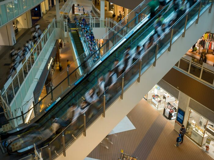 People on escalators in a busy shopping mall showing dynamic scenes behind boring industries.