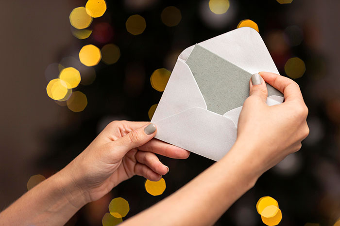 Hands with painted nails opening a white envelope against a blurred background showing warm bokeh lights.