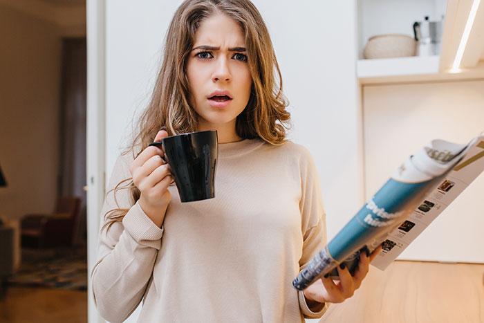 Young woman holding a mug and magazine with a confused expression, capturing the moment attraction ended due to a weird ick.