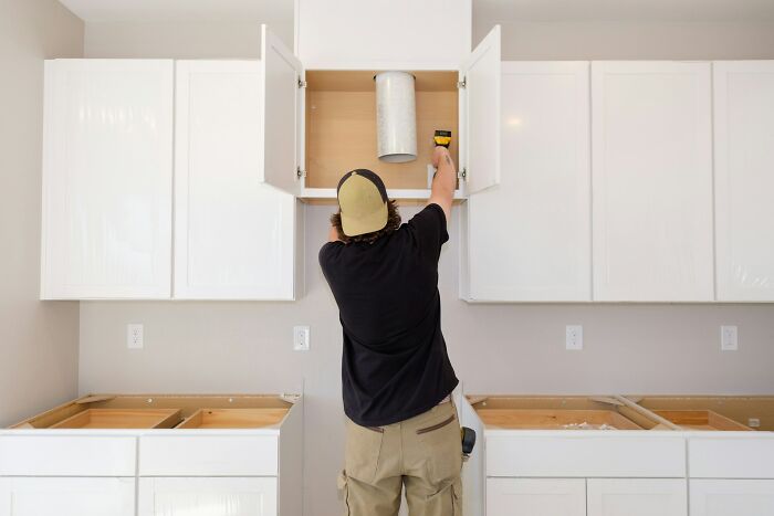 Person measuring inside a kitchen cabinet, illustrating rich people far from reality with unusual home tasks.