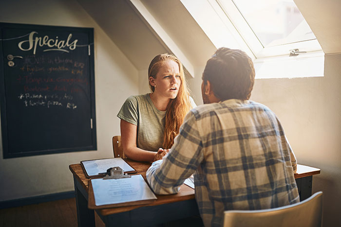 Woman looking frustrated while talking to husband at a table, illustrating complaints about SIL despite free stay. Woman looking frustrated while talking to husband at a table, illustrating complaints about SIL despite free stay.