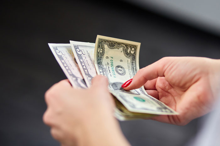 Hands with red nails counting US cash, suggesting tensions between wife and lesbian bestie