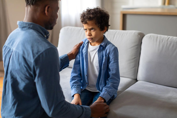 Man suspects wife, father consoling upset young son on couch during serious conversation