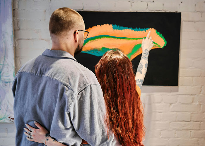 Man with glasses and woman with red hair looking at abstract painting, representing video games and Star Wars figures hobbies.