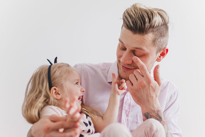 Dad struggling to keep toddler away from mom so she can study, showing playful interaction and family bonding moments.