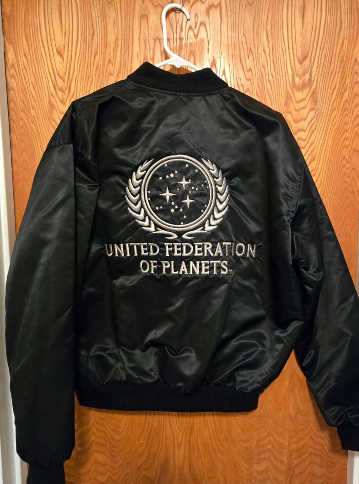 Black jacket with United Federation of Planets logo hanging on wooden door, a weird unexplained sight witnessed by people.