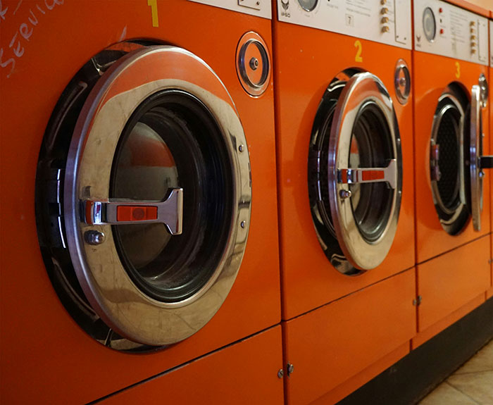 Row of bright orange washing machines with chrome doors in a laundromat setting, evoking weird and unexplained moments witnessed.