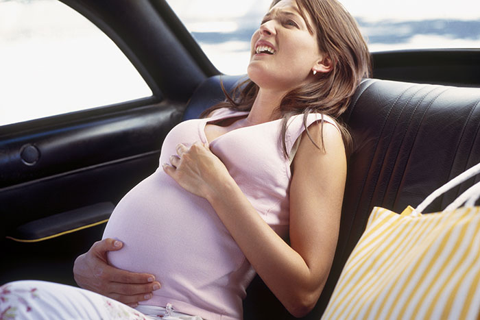 Pregnant woman in car experiencing labor pains, showing distress during an unexpected birth in friends' vehicle.