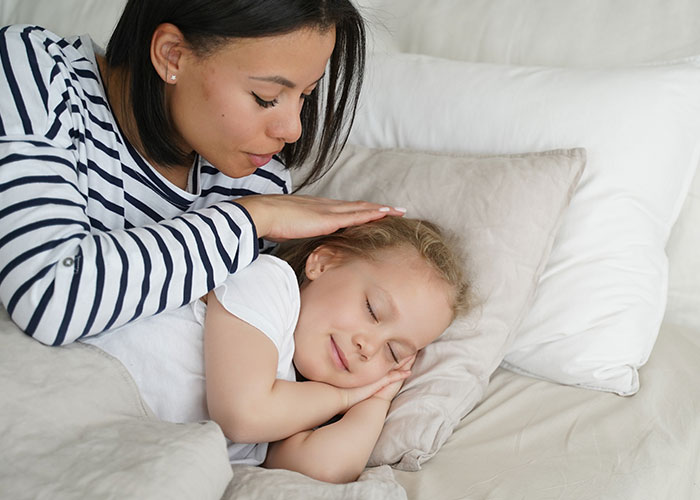 Woman feels treated like unpaid nanny, tenderly comforting sleeping child while lying on a bed at home.