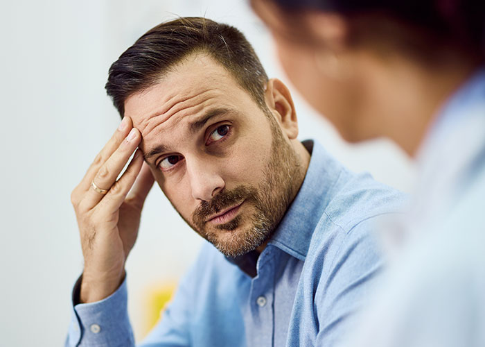 Man in blue shirt looking concerned while listening to a woman, illustrating feelings of being treated like an unpaid nanny.