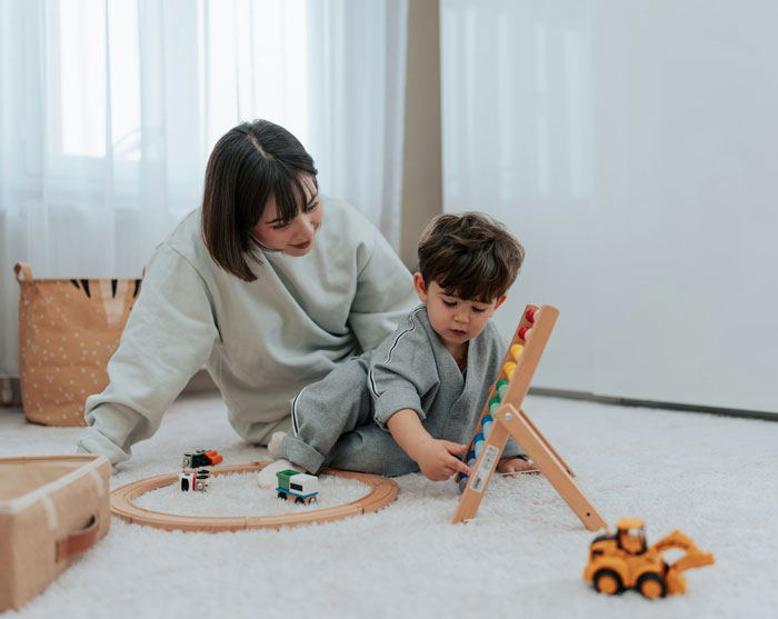 Mom of 6 caring for young child while babysitting with toys scattered, feeling stressed and overwhelmed at home.