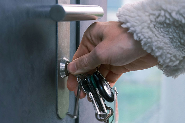 Hand holding keys unlocking an apartment door, representing a man noticing strange things happening inside.