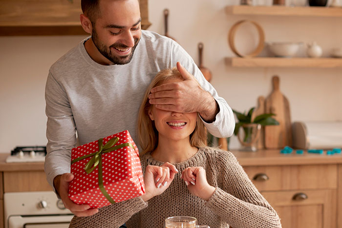 Woman confused about Christmas gifts from boyfriend, surprised by presents while sitting in a cozy kitchen setting.