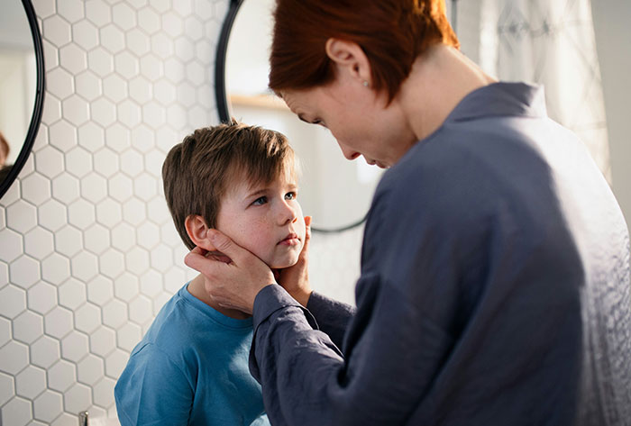 Woman gently holding a young boy&rsquo;s face in a bathroom, illustrating a man torn between husband and mother-in-law.