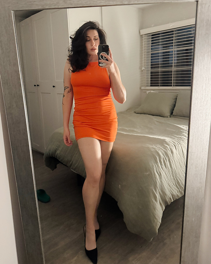 Single woman taking mirror selfie in orange dress, reflecting on her Hinge match with the perfect guy.