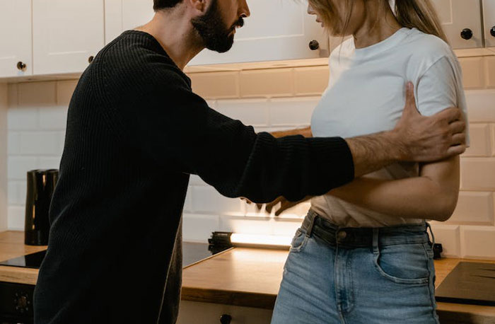Man and woman in kitchen having tense argument, highlighting love is a verb and relationship conflict over food saved for kids.