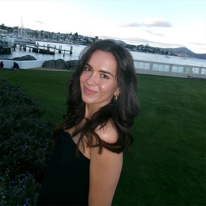 Woman with dark hair smiling outdoors near waterfront, relating to woman stunned by hinge match on first date.