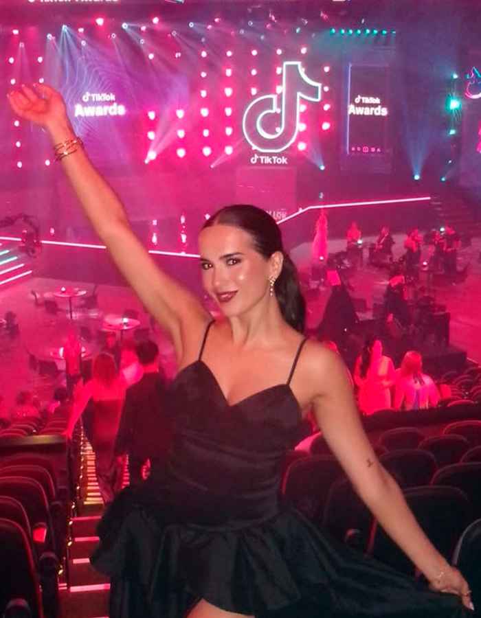 Woman in black dress celebrating at TikTok Awards event with colorful lights in the background, tied to Hinge match first date story.