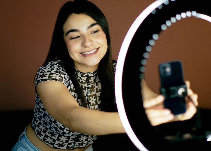 Young woman taking selfies using a ring light and smartphone, illustrating what women obsess over for no reason at all.