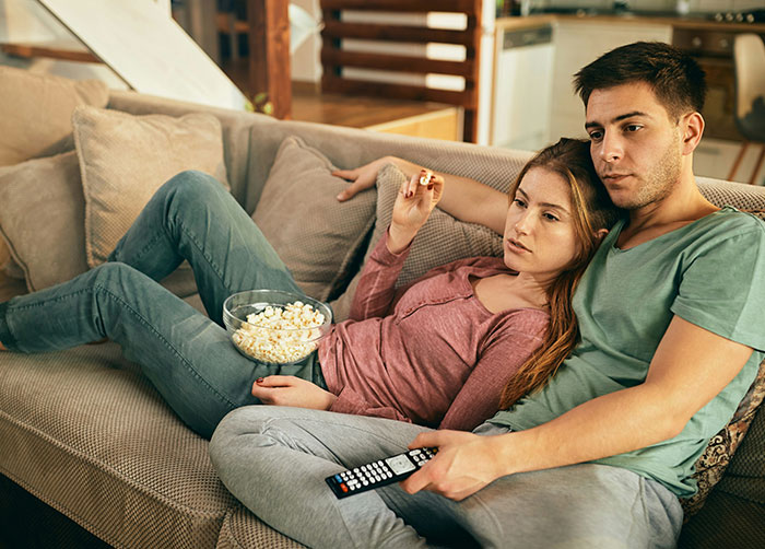 Couple relaxing on a sofa with popcorn, sharing a moment while watching TV, highlighting what women obsess over for no reason.