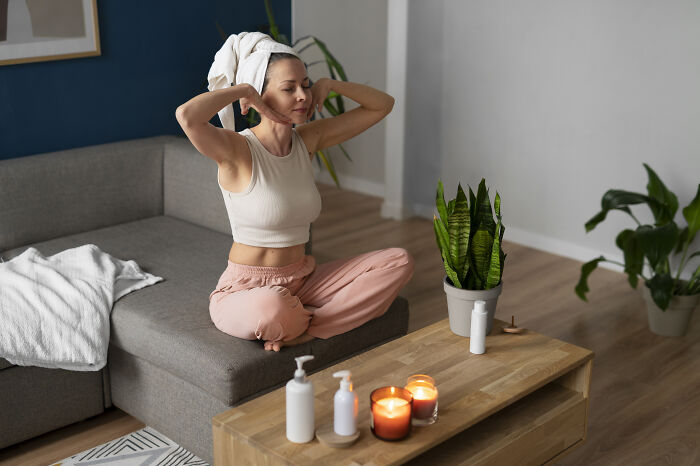 Woman with towel on head relaxing on couch surrounded by skincare products and candles, breaking misconceptions about women.
