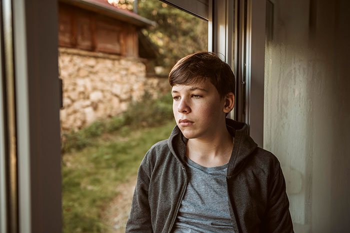 Teen boy looking outside a window, reflecting on lucky times people got out of dangerous situations safely.