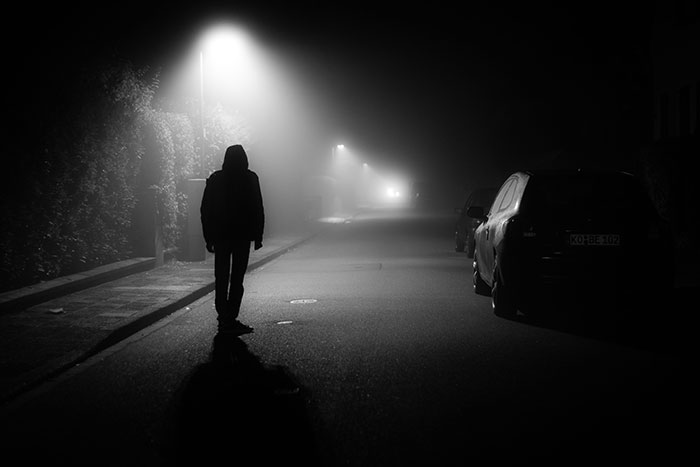 Person walking alone on a dark foggy street at night under a streetlight illustrating lucky escape moments.