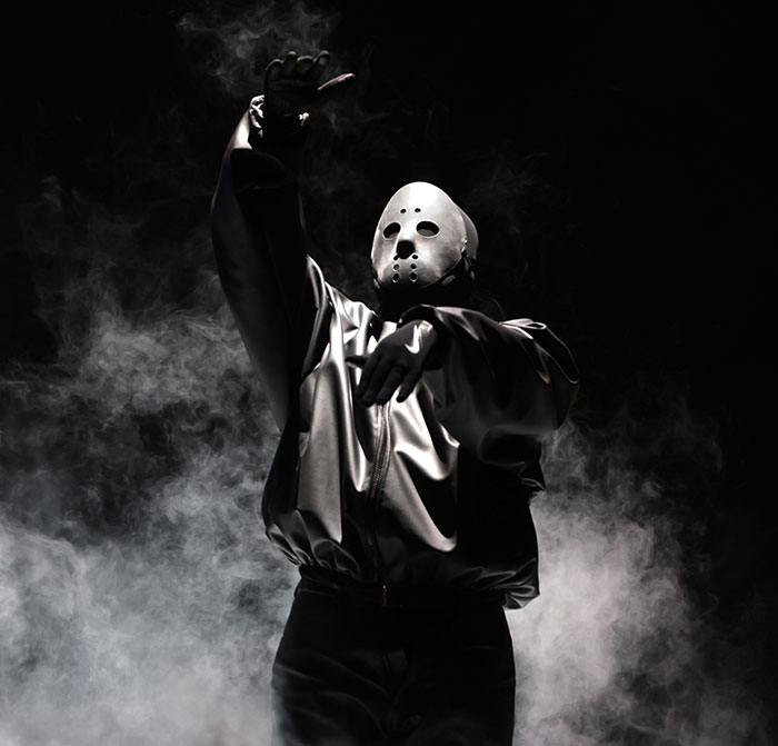 Person wearing white hockey mask and satin jacket posing amid smoke in dark setting, related to Kanye West health battle.