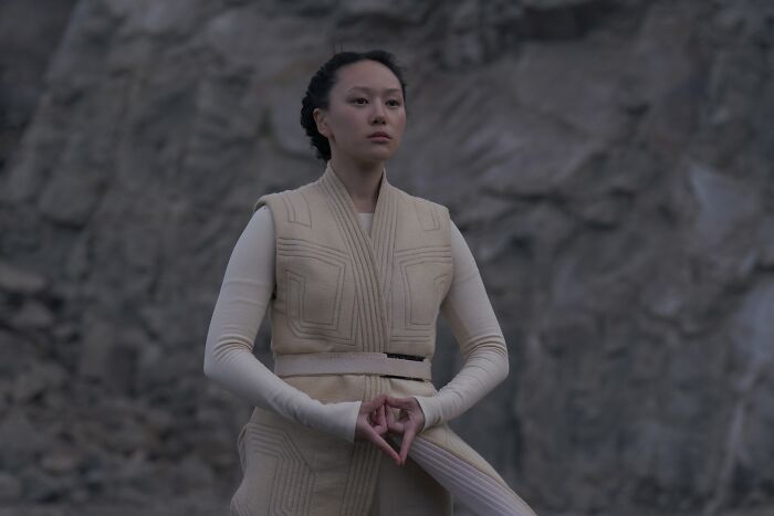 Actress behind Sophie Baek in Bridgerton standing outdoors wearing a beige vest with a rocky background. Actress behind Sophie Baek in Bridgerton standing outdoors wearing a beige vest with a rocky background.