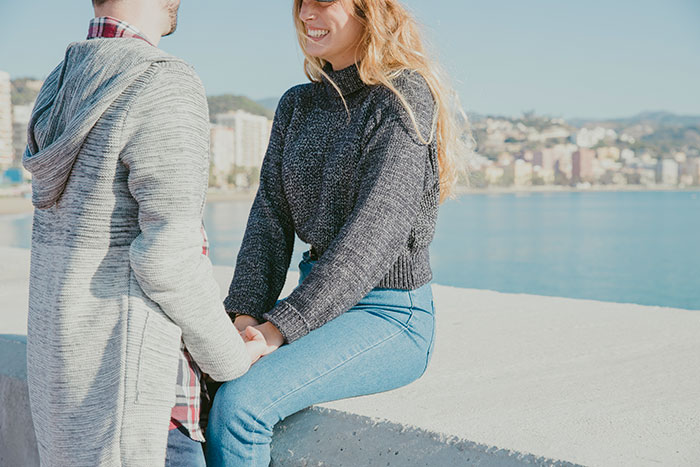 Couple holding hands outdoors by water with woman smiling, illustrating SAHM wife and financial problems theme.