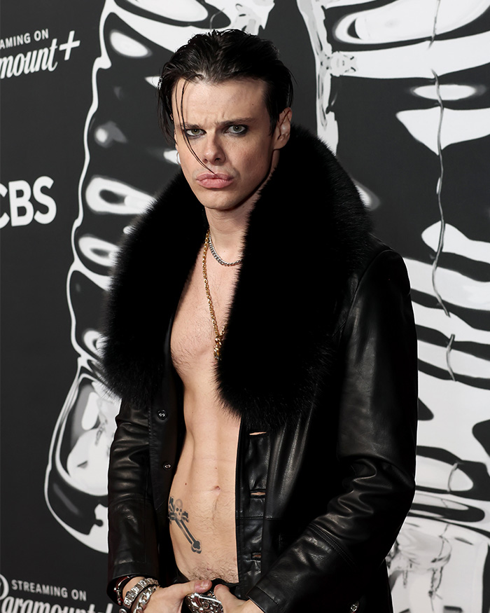 Unclothed rock star Yungblud wearing a black fur-collared leather jacket at a Sydney yacht party event. Unclothed rock star Yungblud wearing a black fur-collared leather jacket at a Sydney yacht party event.