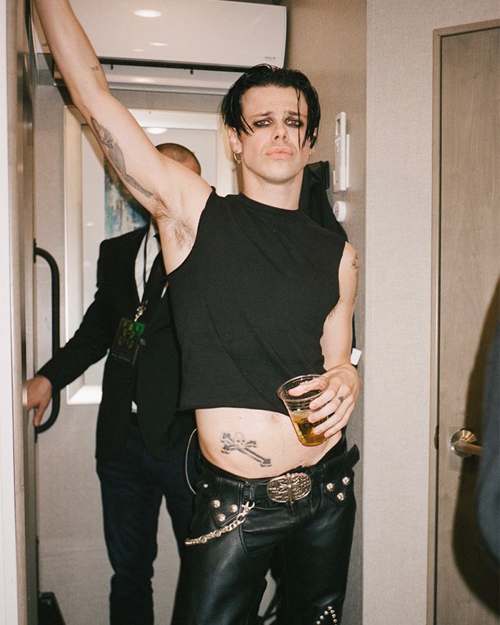 Rock star Yungblud in black sleeveless top and leather pants holding a drink while partying indoors at a Sydney yacht event. Rock star Yungblud in black sleeveless top and leather pants holding a drink while partying indoors at a Sydney yacht event.
