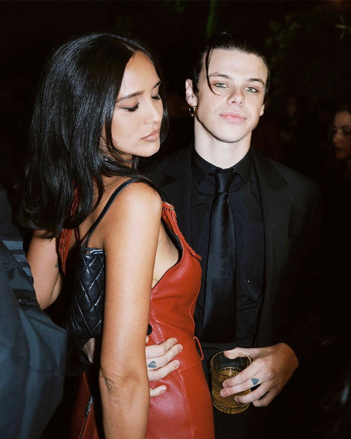 Yungblud dressed in black suit holding a drink, partying with a woman in red dress at a wild Sydney yacht bash. Yungblud dressed in black suit holding a drink, partying with a woman in red dress at a wild Sydney yacht bash.